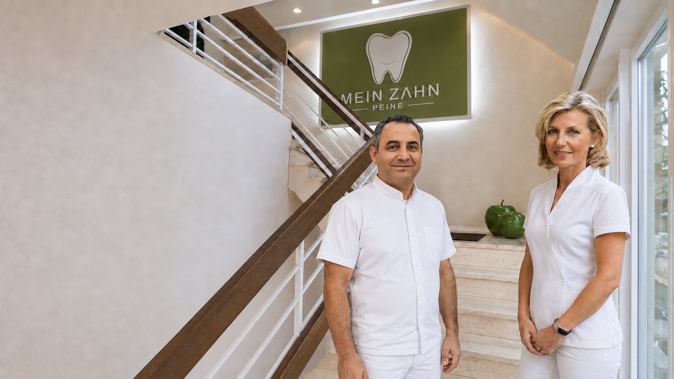 Zahnarzt Reza Yamini und Zahnärztin Dr. Stefanie Morich-Rademacher im Treppenhaus der Zahnarztpraxis Mein Zahn Peine vor dem Praxisschild